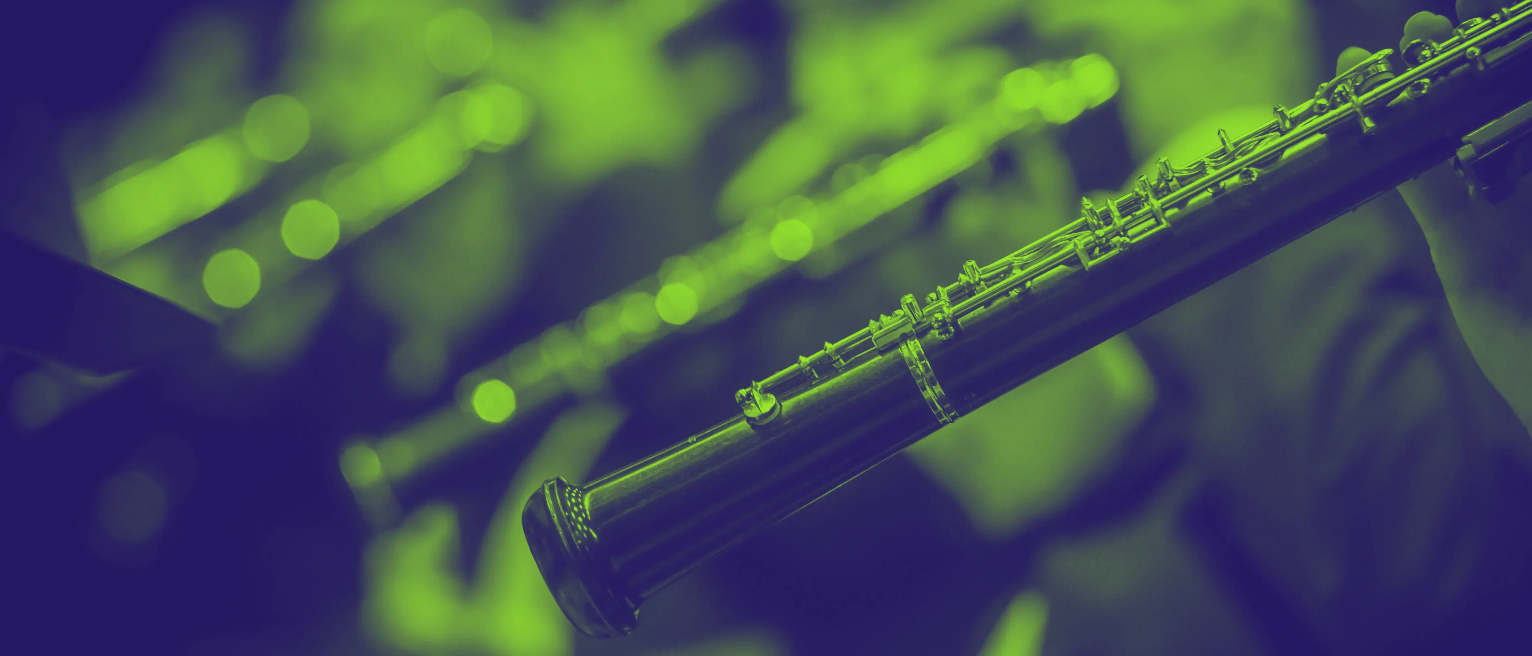 Vier Klarinetten, die von den Orchestermusiker*innen nebeneinander sitzend gespielt werden. Die erste Klarinette ist im Fokus, die anderen verschwimmen. Das Bild ist mit einem grellgrün-dunkelvioletten Buoton-Filter eingefärbt.