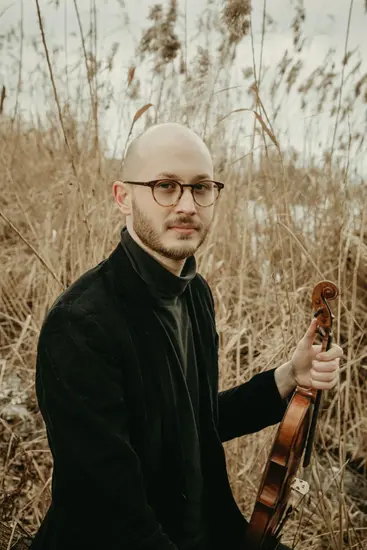 Moritz Ter-Nedden in Aufnahme ab Oberkörper in schwarzer Kleidung mit einer Violine in der Hand in einem Weizen - und Gräserfeld.