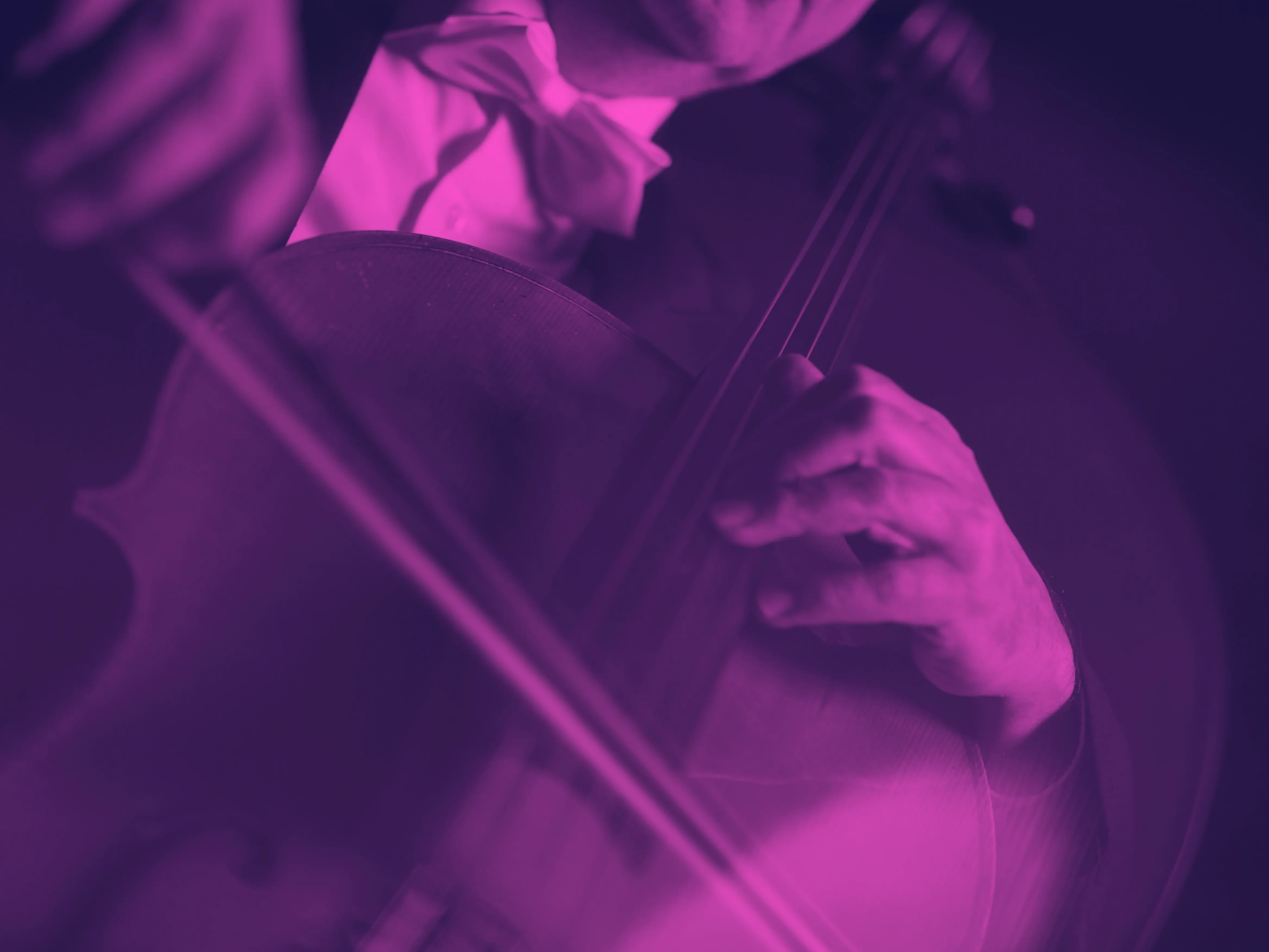 Nahaufnahme auf eine Person, die Violoncello spielt. Der Fokus liegt auf dem Instrument. Das Bild ist mit einem pink-dunkelvioletten Duoton-Filter eingefärbt.