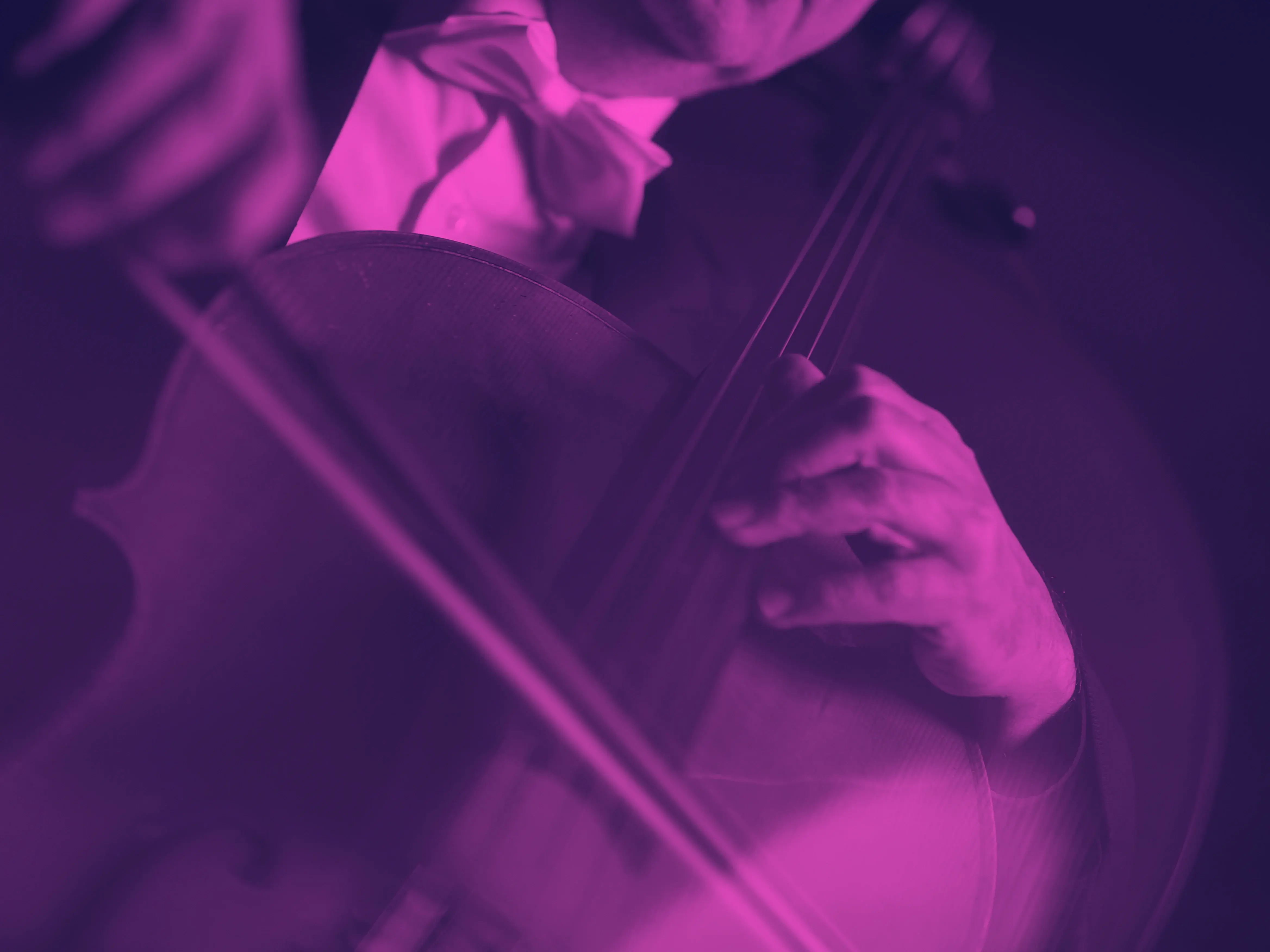 Nahaufnahme auf eine Person, die Violoncello spielt. Der Fokus liegt auf dem Instrument. Das Bild ist mit einem pink-dunkelvioletten Duoton-Filter eingefärbt.