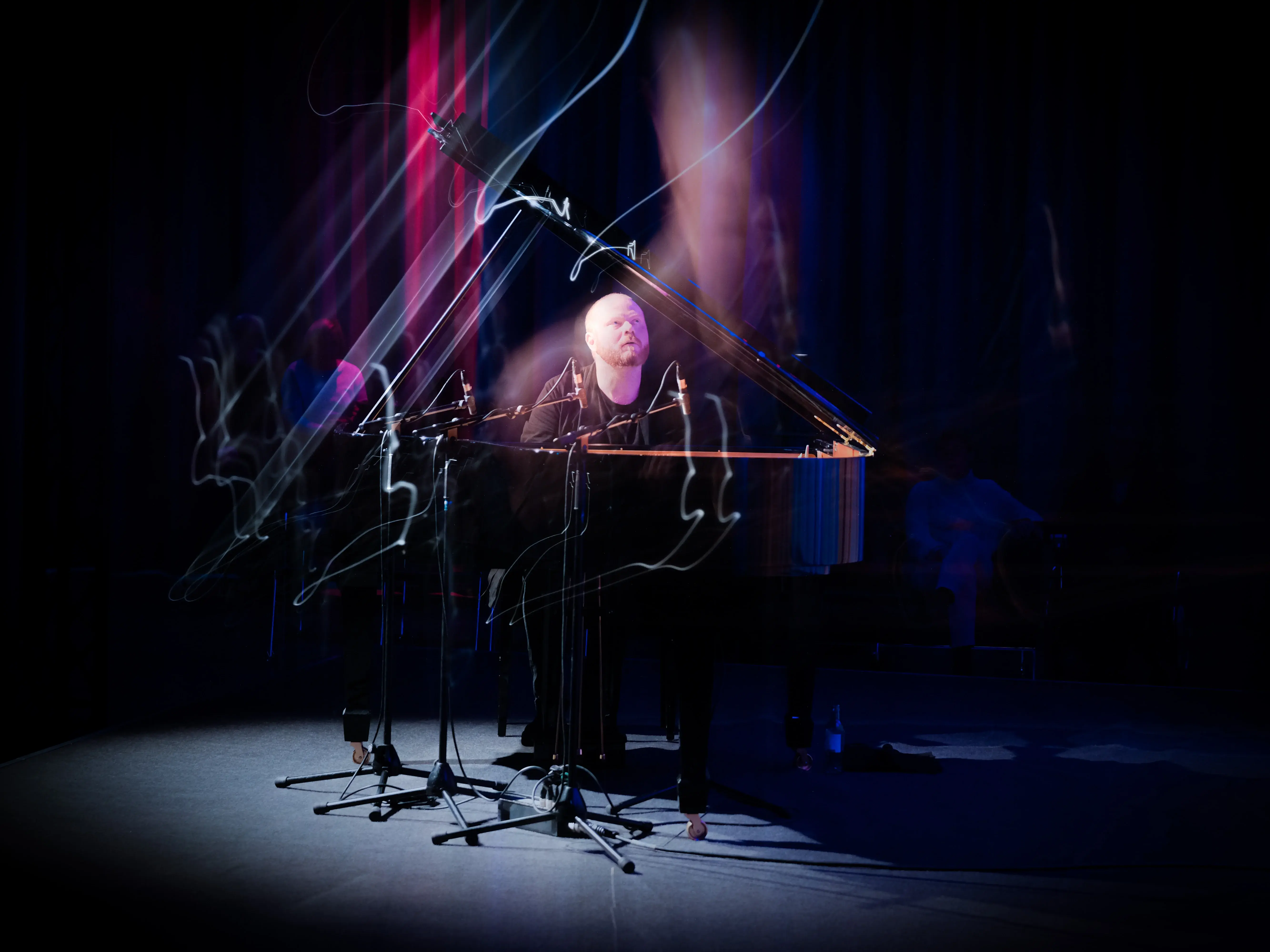 Dekoratives Foto für das Konzert mit Kai Schumacher. Kai Schumacher am Flügel sitzend während des Spielens. Der Hintergrund ist dunkeln, angeleuchtet wird nur Kai Schumacher und sein Instrument.