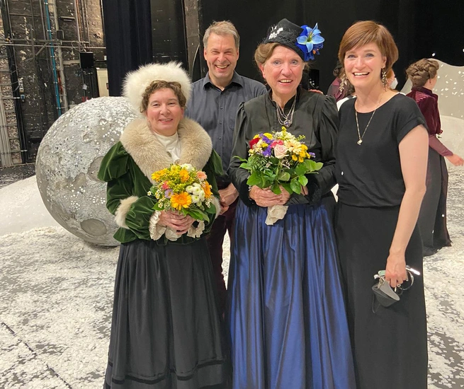 Vier Personen stehen auf der Bühne im Stadttheater und lächeln in die Kamera. Zwei Personen halten einen Blumenstrauß in der Hand.
