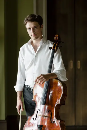 Foto von Cellist Alexander Warenberg, stehend mit Celli in der linken Hand. 
