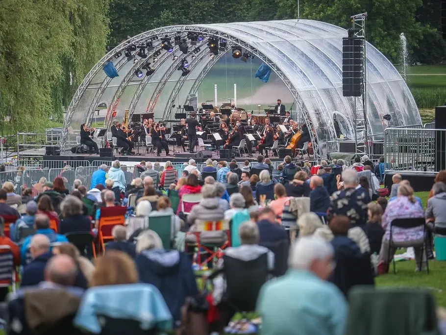 Foto von einer Outdoor-Bühne im Bielefelder Bürgerpark, davor sitzt Publikum. Titelbild für das vielHarmonie Open-Air-Konzert.
